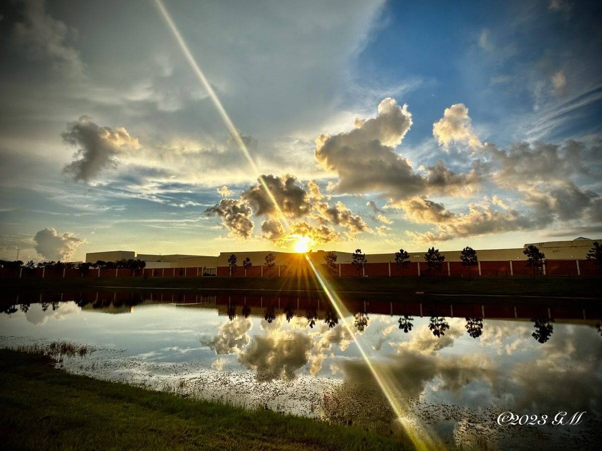 Sun rising over a building and pond with clouds in the sky