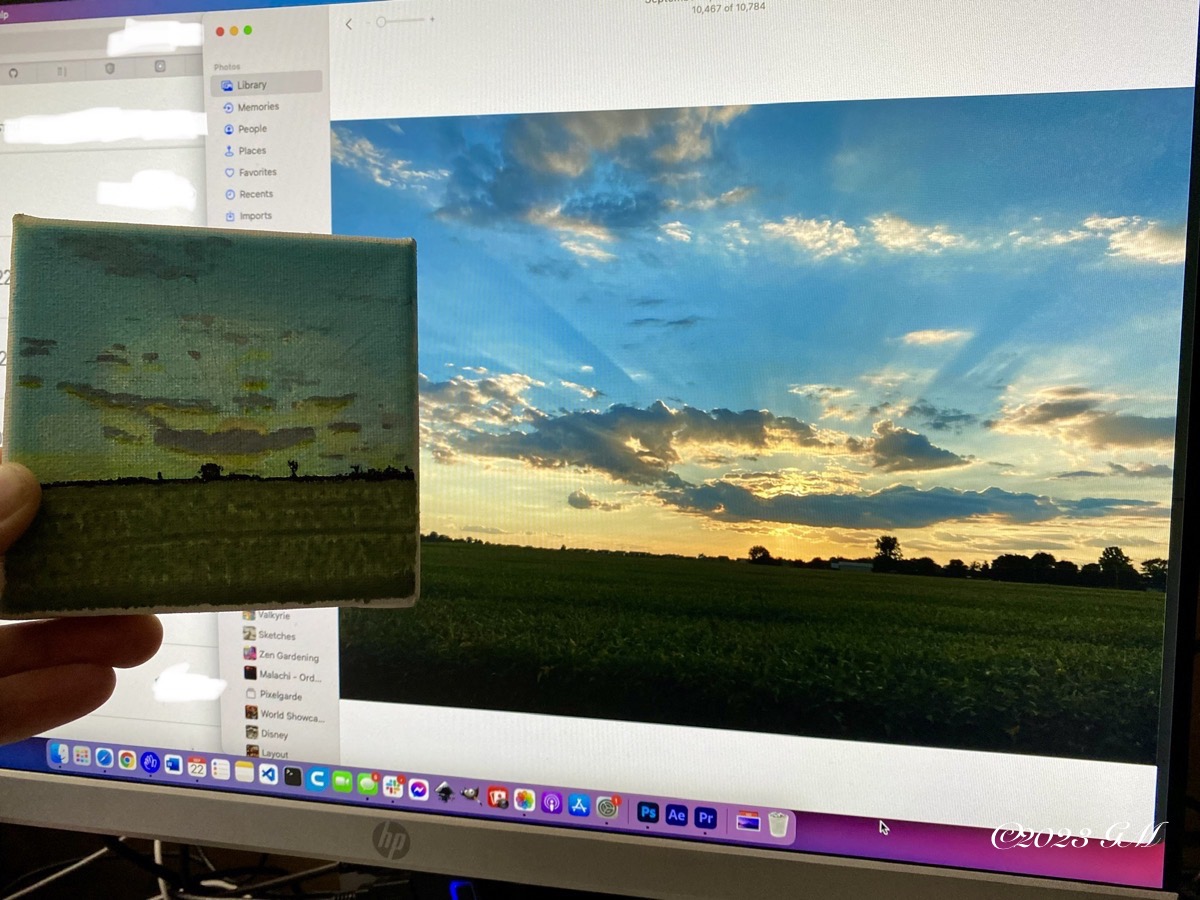 The final painting held up in front of the reference photo of the sunset